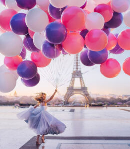 girl in dress with large amount of pink and purple balloons in Paris, France with eiffel tower in background